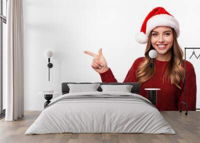  Beautiful young woman with Santa hat looking at camera pointing finger away at copy space Wall mural