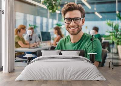 cheerful man with glasses and a green t-shirt is smiling at the camera, seated in a modern office wi Wall mural