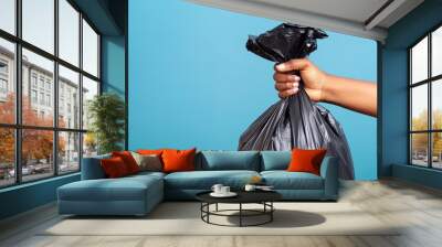 Closeup woman hand throwing away black polyethylene garbage bag on isolated blue background with space for copy  Wall mural