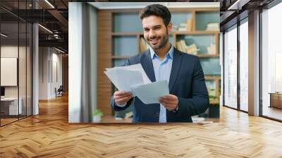 Happy young Latin business man checking financial documents in office. Smiling male professional account manager executive lawyer holding corporate tax bill papers standing at work Wall mural