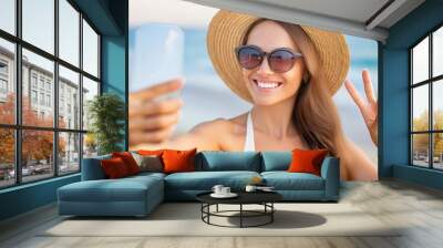 Happy young woman in straw hat and sunglasses takes a selfie on the beach  Wall mural