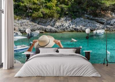 Young woman in beach clothes and sun hat looking at beautiful beach with boats and turquoise sea Wall mural