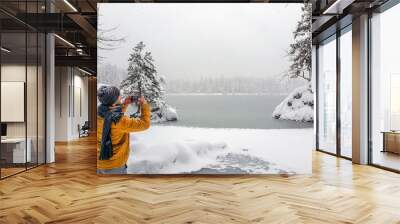 View of a young male taking a photo of a frozen lake Wall mural