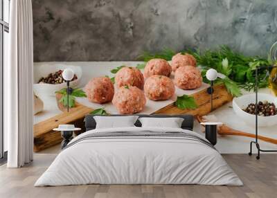 Minced raw meatballs with greens on a wooden board on a light-colored table Wall mural