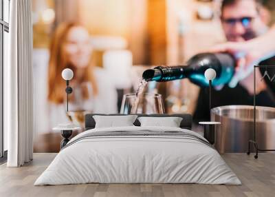 Waiter pouring wine in glass for guests at table in bar restaurant party Wall mural