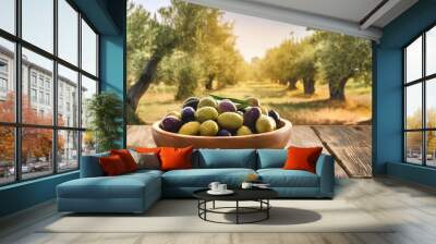 ripe olives in a wooden plate on a wooden table against the backdrop of an olive grove, copy space Wall mural