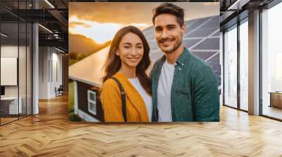 Smiling young couple standing in front of their home with solar panels on the roof in the evening Wall mural