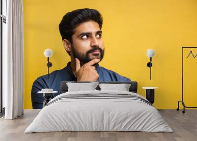 Thoughtful bearded indian man holding hand on chin looking interested aside at copy space isolated on yellow background thinking of new job opportunities, having doubt question or deciding concept Wall mural