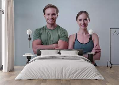 Young smiling man and woman in athletic wear standing with arms crossed on a white background Wall mural