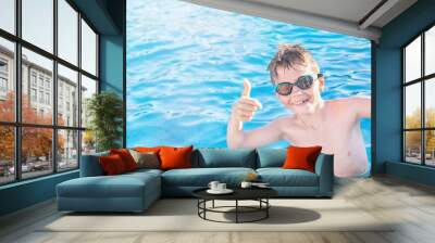 Healthy lifestyle. Active, happy nine years old child (boy) in sport goggles showing thumbs up on the swimming pool background. Kid learning to swim, enjoying water. Swimming activities for children. Wall mural