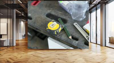 Detailed photo of the table in the workshop. We see a tape measure, a pencil and a cutting knife. Wall mural