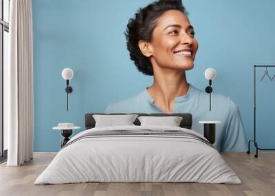 Portrait of a blissful indian woman in her 40s donning a classy polo shirt in front of pastel blue background Wall mural