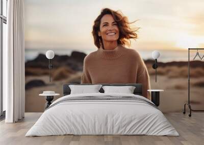 Portrait of a cheerful woman in her 40s dressed in a warm wool sweater on beautiful beach sunset Wall mural