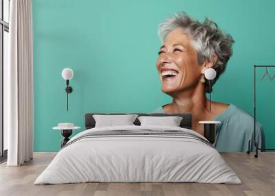 Portrait of a cheerful woman in her 60s laughing on pastel green background Wall mural