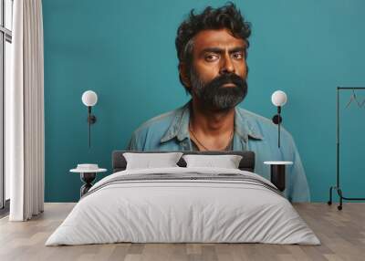 Portrait of a glad indian man in his 40s wearing a rugged jean vest in pastel teal background Wall mural