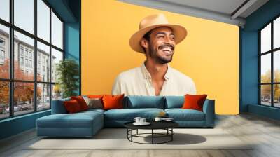 Portrait of a grinning indian man in his 20s donning a classic fedora in front of soft yellow background Wall mural