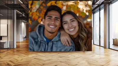 Portrait of a grinning latino couple in their 20s dressed in a comfy fleece pullover in front of background of autumn leaves Wall mural