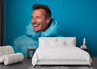 Portrait of a grinning man in his 40s sporting a quilted insulated jacket isolated in soft blue background Wall mural