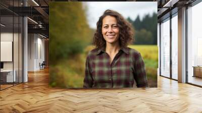 Portrait of a grinning woman in her 40s dressed in a relaxed flannel shirt in quiet countryside landscape Wall mural