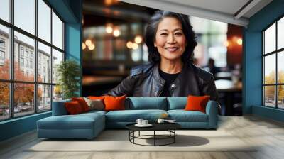 Portrait of a happy asian woman in her 60s sporting a classic leather jacket isolated on bustling restaurant background Wall mural