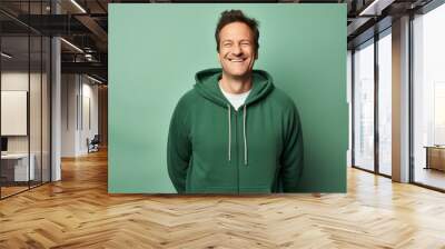 Portrait of a happy man in his 40s wearing a zip-up fleece hoodie in front of soft green background Wall mural