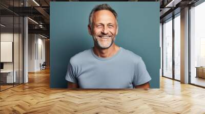 Portrait of a happy man in his 50s dressed in a casual t-shirt in front of pastel gray background Wall mural