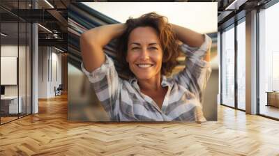 Portrait of a happy woman in her 40s dressed in a relaxed flannel shirt while standing against relaxing hammock on the beach background Wall mural