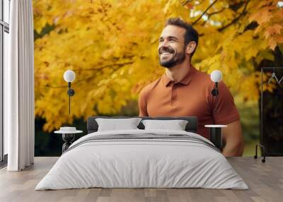 Portrait of a joyful man in his 30s wearing a sporty polo shirt in background of autumn leaves Wall mural