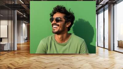 Portrait of a smiling indian man in his 20s wearing a trendy sunglasses against a soft green background. AI Generation Wall mural