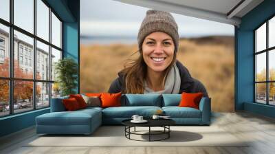 Portrait of a smiling woman in her 30s sporting a trendy beanie over serene dune landscape background Wall mural