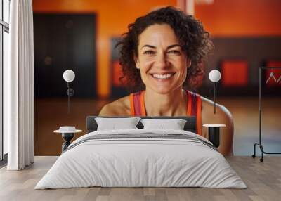 Portrait of a smiling woman in her 40s dressed in a high-performance basketball jersey in front of vibrant yoga studio background Wall mural