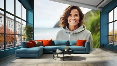 Portrait of a smiling woman in her 40s sporting a comfortable hoodie isolated on tropical island background Wall mural