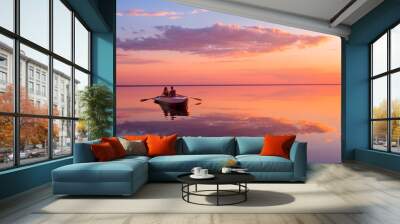 A couple in love look at beautiful sunset in a rowing boat on the lake. Pink sky and vanilla clouds. Romantic scene - lovers ride a boat in nature during sunset. Amazing landscape with people Wall mural