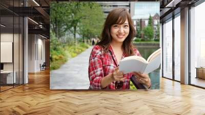 Young asian woman reading a book in a park Wall mural