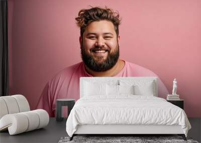 Happy young man with overweight and beard isolated on a pink background, looks into the camera and smiles. Fat guy in a pink shirt Wall mural