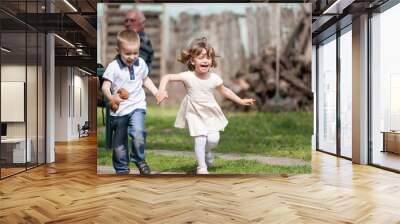 Happy little girl and a boy running while holding hands Wall mural