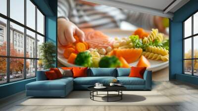 A close-up side view captures a plate filled with a nutritious meal for a baby practicing self-feeding through baby-led weaning. The dish includes salmon, vegetables, pasta, and fruit Wall mural