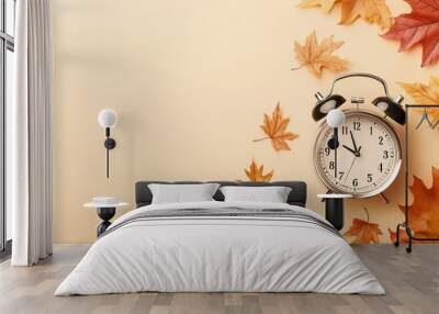 An alarm clock surrounded by autumn leaves on a beige background, symbolizing the seasonal time change. The scene evokes the 