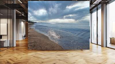 Empty coast of Baltic Sea with calm waves rolling on sand beach under dramatic sky with stormy clouds and sun rays. With no people seaside landscape. Wall mural