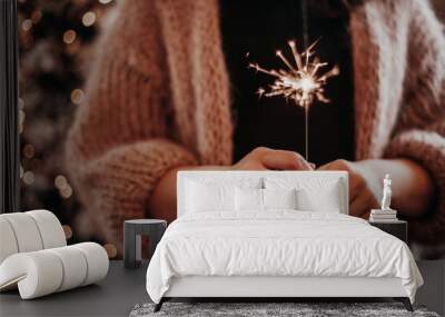 Closeup of a woman holding a sparkler miracle candle in a cozy winter sweater. Bokeh Christmas light background. Cozy Christmas mood. Wall mural