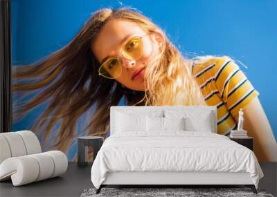 happy teenage attractive girl looks into the camera on the sunny beach over the blue sky wearing yellow sunglasses. Wall mural