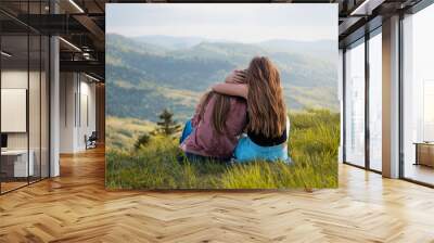 Two friends hugging looking at the Carpathians mountains. Two girls on top of the mountain watching at sunset. Wall mural