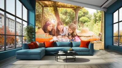 Three teenage girls reading magazine while lying in tree house in summer Wall mural