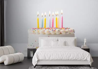 Birthday cake with colorful candles and sprinkles sits on a white background. Wall mural