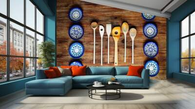 Detail of wooden cooking spoons and painted ornate plates on textured wooden table, vintage style Wall mural