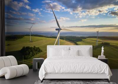 Aerial view of wind turbine farm. Wind power plants in green landscape against sunset sky with clouds. Aerial, drone inspection of wind turbine. Wall mural