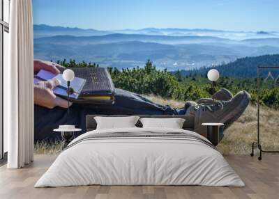 Outdoor Bible study during mountain hike. Female hands holding a Bible on the knees during outdoor devotion and Bible study in the mountains. Mountaintop outlook with high sky. Copy space. Wall mural