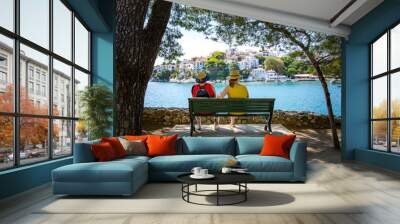 Two Women sitting on a bench overlooking a beautiful mediterranean harbour on a sunny summer day Wall mural