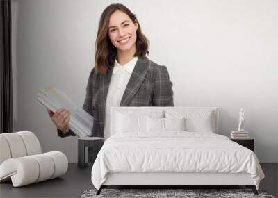 Beautiful and smiling business woman with paperwork in hands, standing isolated on white, looking happy about the papers she's holding and smiling in to the camera.  Wall mural