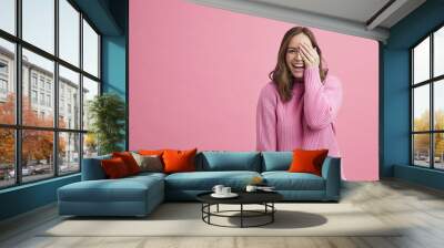 Happy beautiful woman holding her hand infront of her eye wearing all pink on a pink colorful background Wall mural